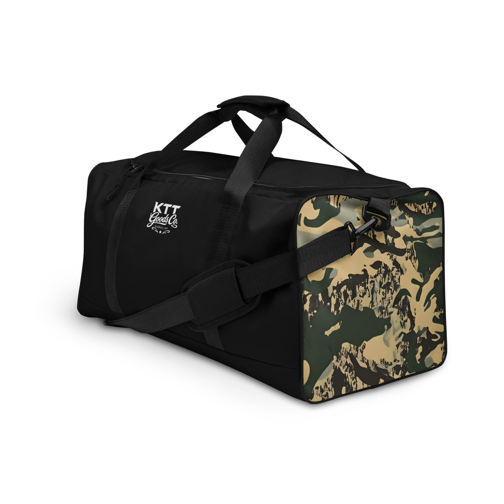 Left-front view of the TV-D1 Field Duffle Bag showing the single white KTT Goods Co. mark and a TV-D1 camouflage side panel.